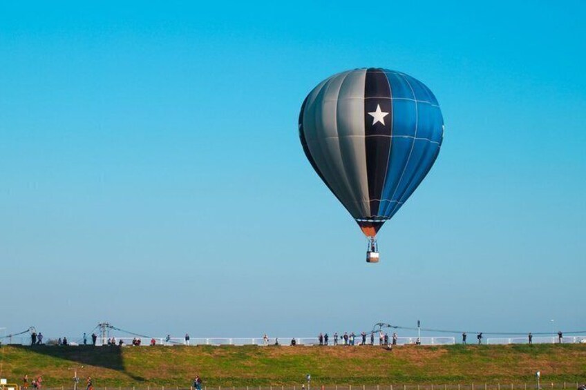 A hot air balloon with a star design flying over a grassy field. 4