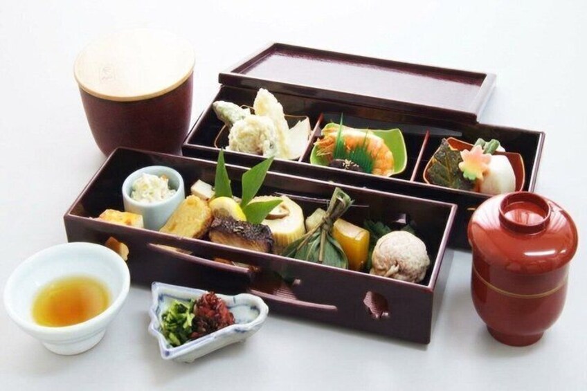 A traditional Japanese bento box with various food items and a small bowl of soy sauce. 1