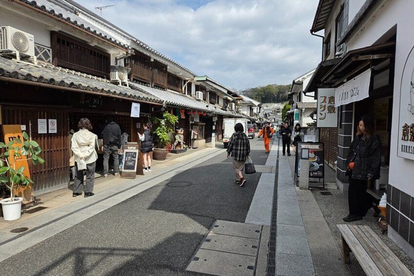 A street in a traditional Japanese town with wooden buildings, pedestrians, and signage. 3