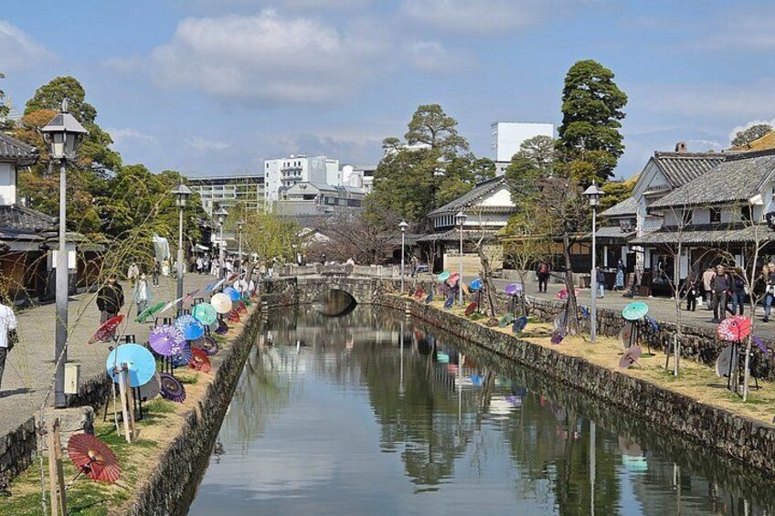 A canal with traditional buildings on either side, a row of colorful umbrellas, and a clear sky. 4