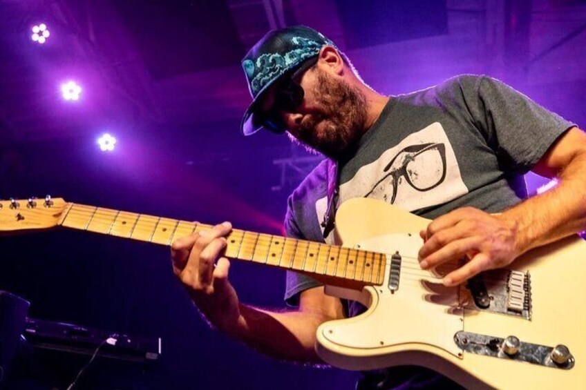 A person playing an electric guitar on stage with purple lighting. 1