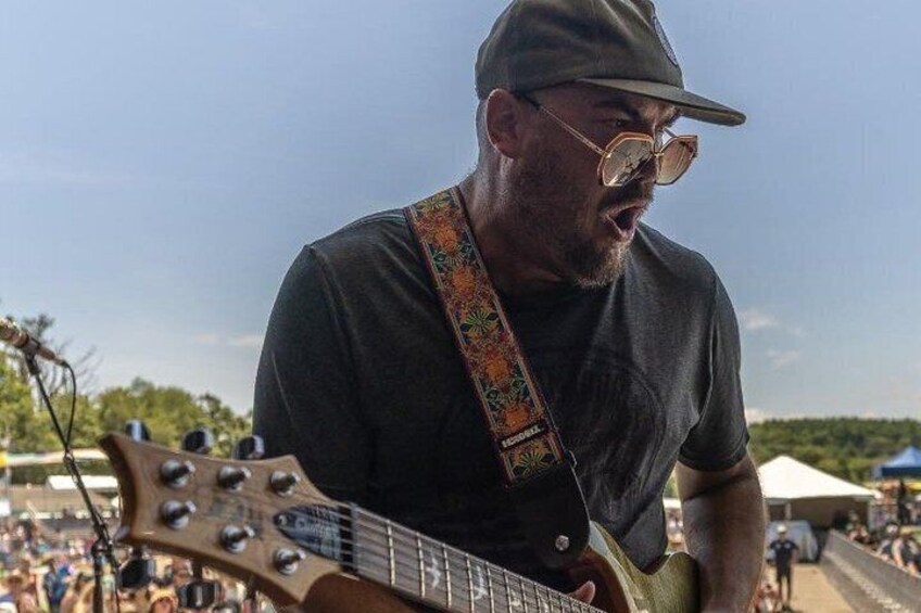 A person playing a guitar at an outdoor event with a crowd in the background. 3