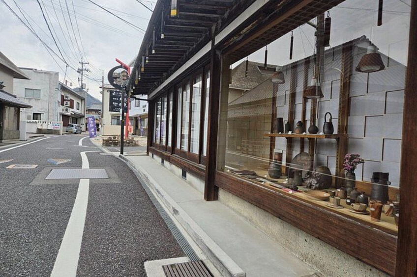 En gade med traditionel japansk arkitektur, et butiksvindue med keramik og en tydelig vej med skilte. 3