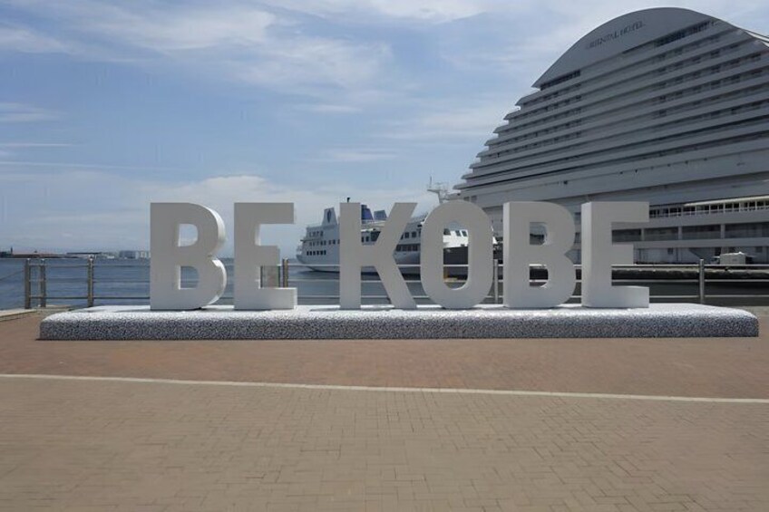 A large sign with 'BEKOBE' in white letters, a modern cruise ship, and a waterfront. 5