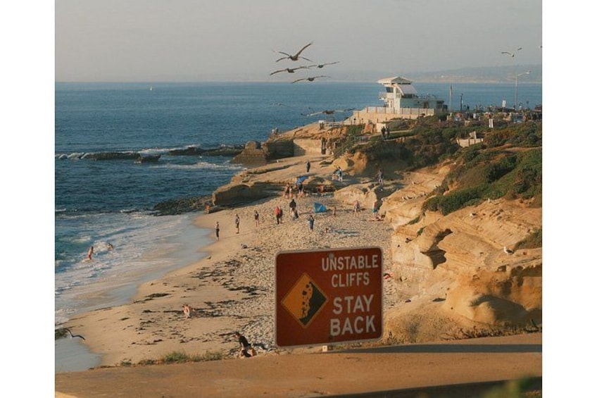 A beach with a warning sign for unstable cliffs and a lifeguard tower in the background. 4