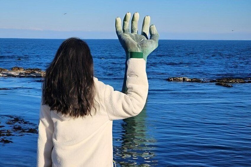 A person wearing a white jacket and green gloves standing in water with a rocky shoreline in the background. 4