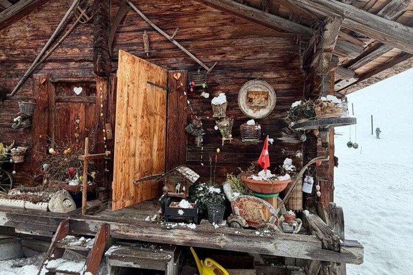 A rustic wooden cabin with a snow-covered porch, decorated with various items and plants. 5