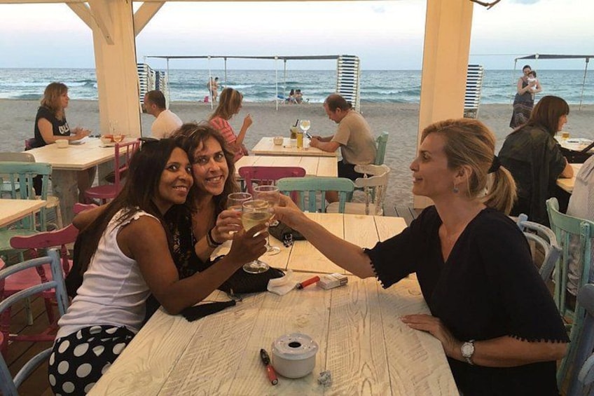 A beachside restaurant with outdoor seating, people dining, and the ocean in the background. 1
