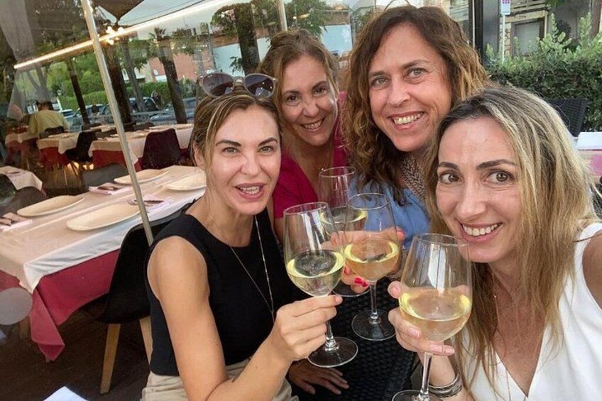 A group of people sitting at an outdoor table with wine glasses. 4