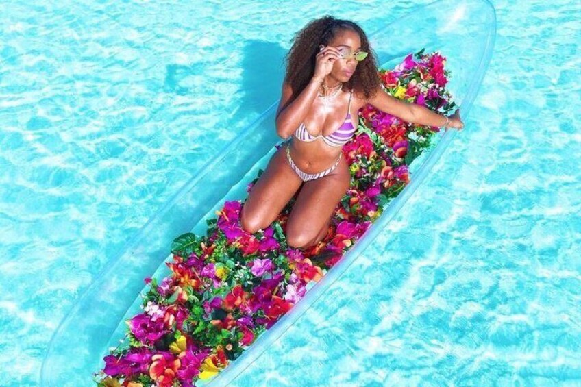 A person in a bikini lying on a floating platform in a pool, surrounded by colorful flowers. 3