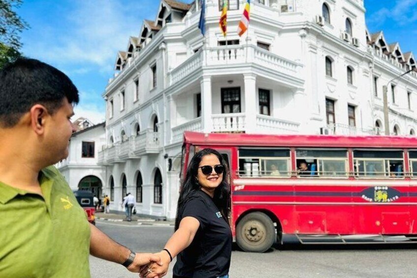 A red double-decker bus, a white historic building, and a person holding hands with another. 1