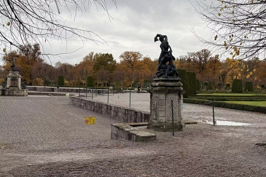 A statue in a park with a gravel path and trees in the background. 5