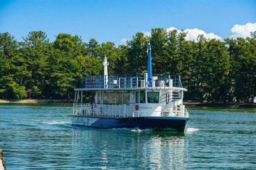 A white and blue boat with a cabin and a mast, moving on a calm river with trees in the background. 5