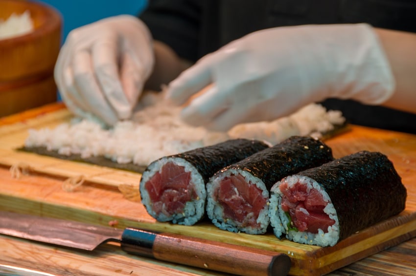 A person preparing sushi rolls with rice and fish on a wooden board. 3