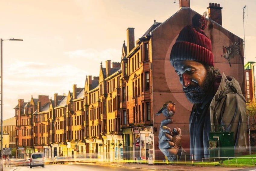 Calle con edificios tradicionales y un mural grande de una persona sosteniendo un pájaro. 2