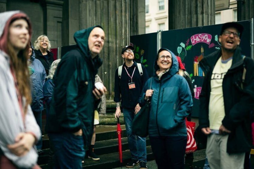 A group of people standing on steps in front of a building with a sign that says 'Glasgow.' 2