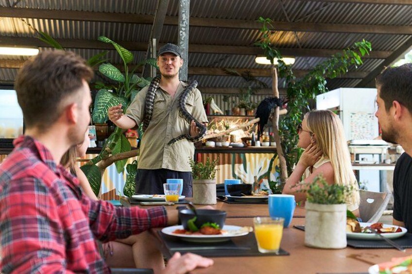 A group of people dining at an outdoor restaurant with a person holding a snake. 2
