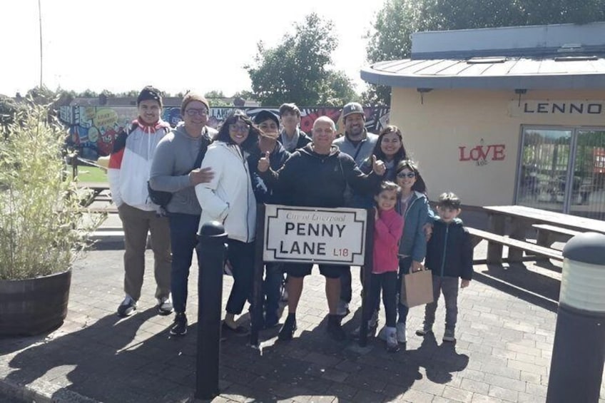 En grupp människor som står framför en skylt med texten ”Penny Lane”. 5