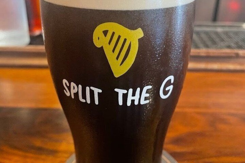 Een glas donker bier met een geel logo van een harp en de tekst 'SPLIT THE G'. 5