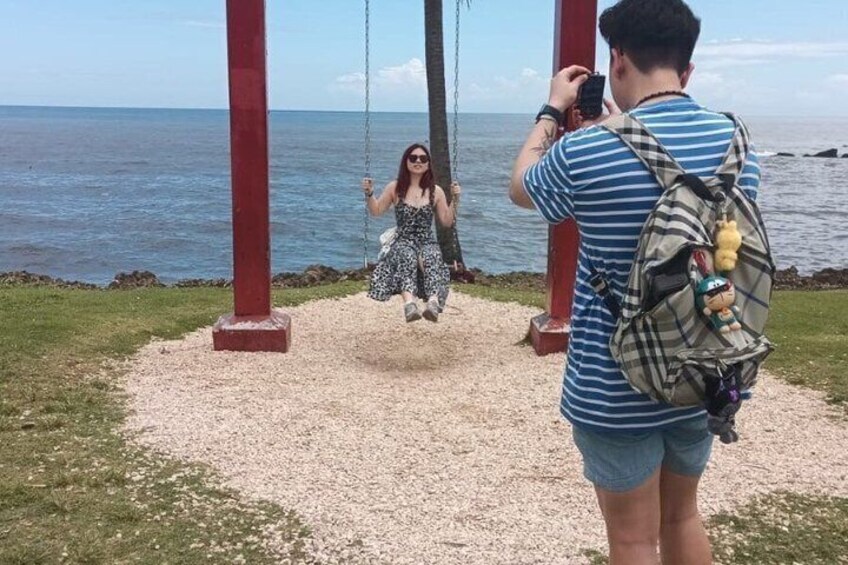 Eine Person schwingt, eine andere Person macht ein Foto, und im Hintergrund ein Strand mit dem Meer. 1