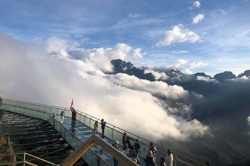 A glass observation deck with people observing clouds and mountains. 3