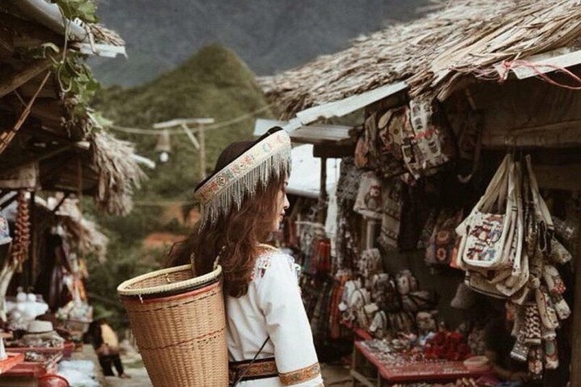 A person carrying a basket, a market stall with patterned bags, and a mountainous landscape in the background. 2