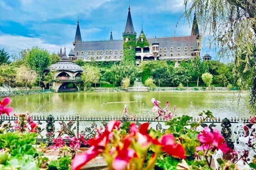 A castle with multiple spires, a pond, and a gazebo in a garden. 1