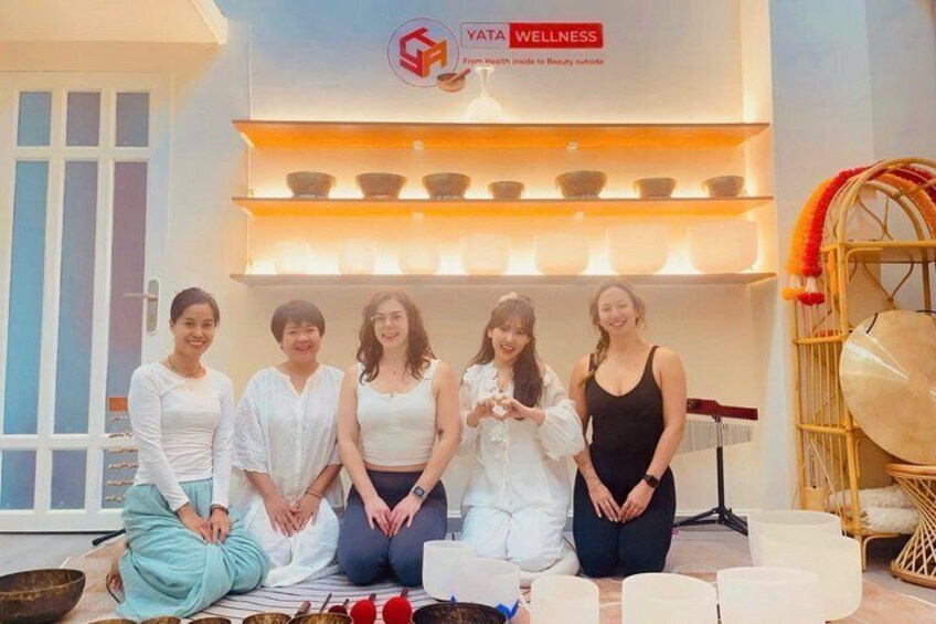 A group of people in a wellness center with a sign reading 'YATA WELLNESS' and a display of bowls and a drum. 5