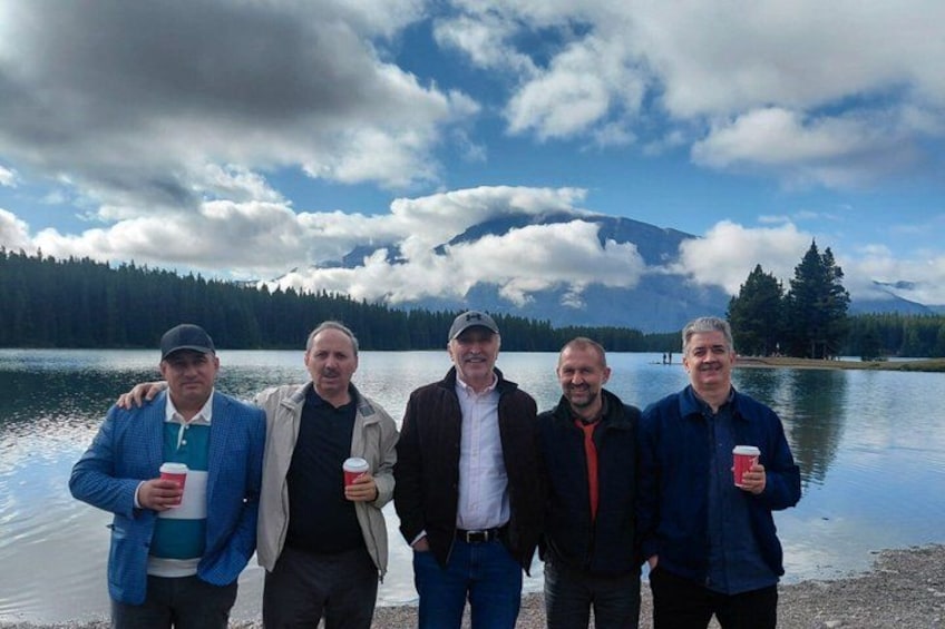 A group of people standing by a lake with mountains in the background. 5
