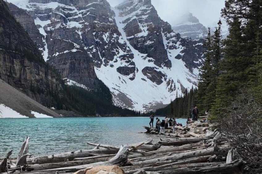 A mountainous landscape with a lake, snow-capped peaks, and a group of people by the water's edge. 3