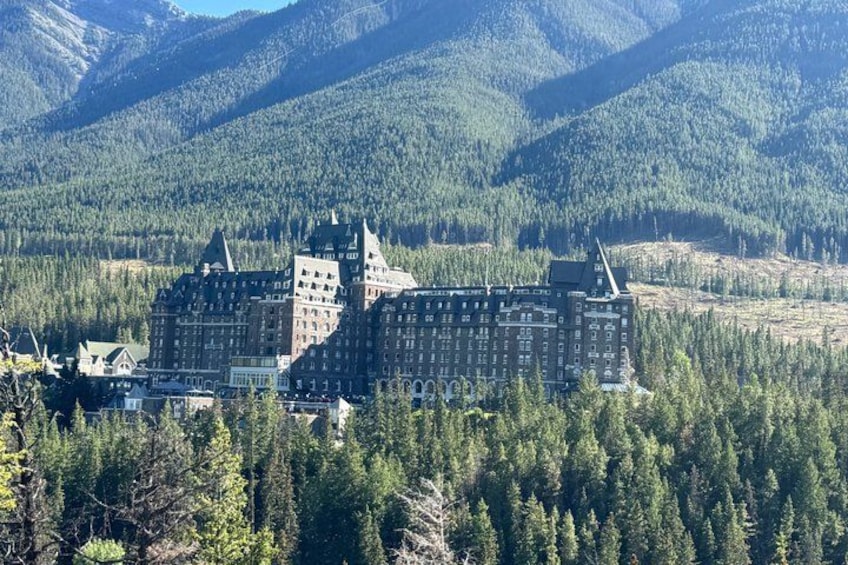 A large, historic building surrounded by dense forest and mountains. 2