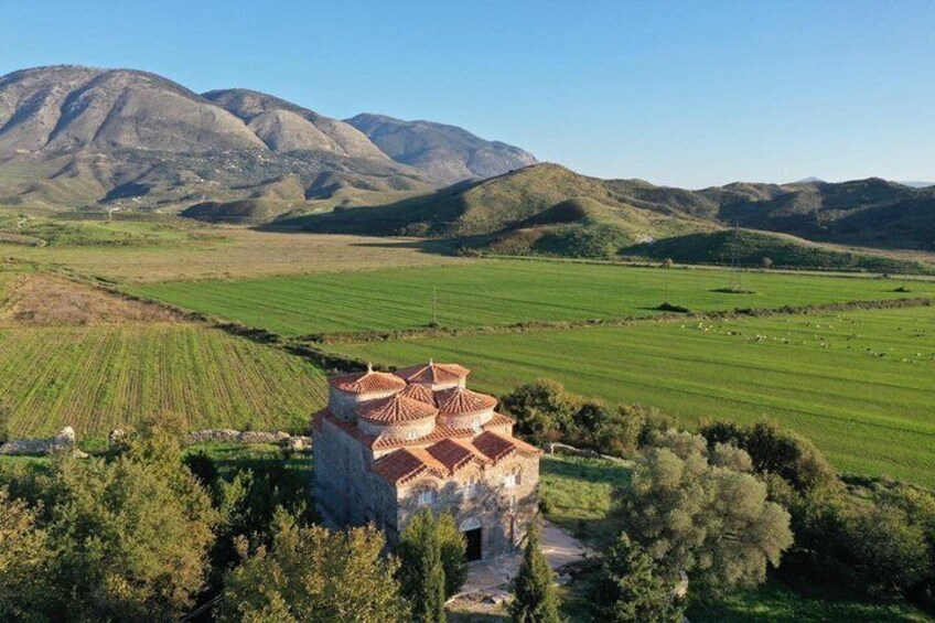 A rural landscape with terraced fields, a stone building with a tiled roof, and mountains in the background. 2