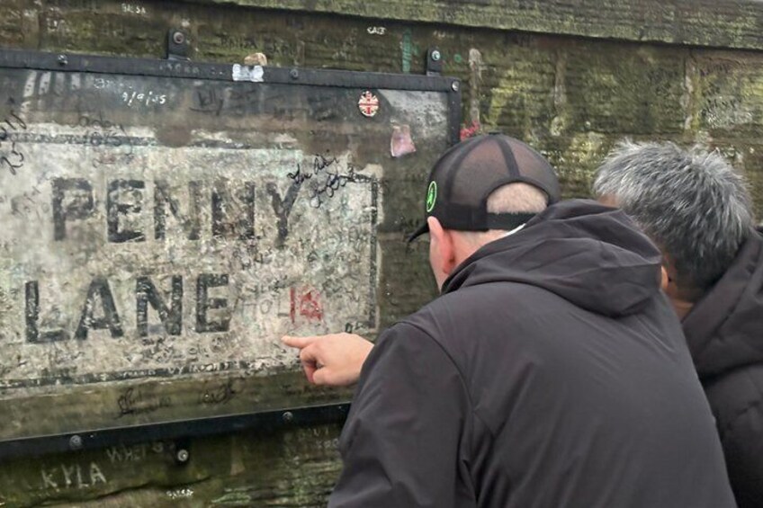 A weathered sign with 'PENNY LANE' written on it, mounted on a metal structure. 1