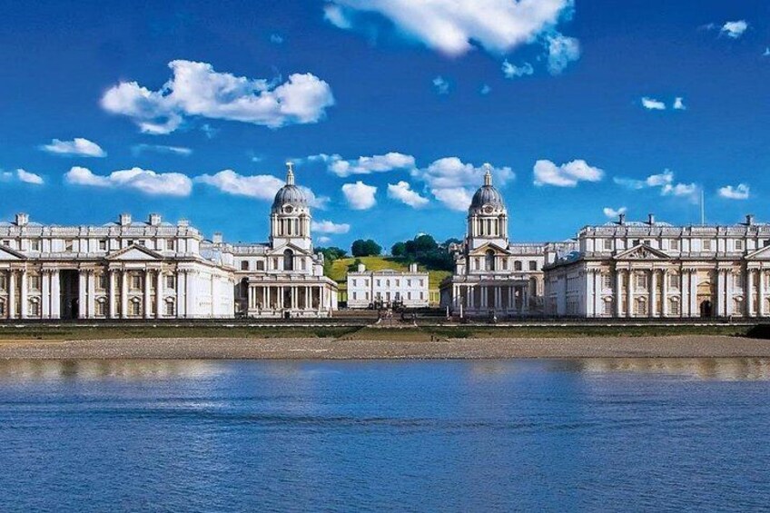 A large classical building with two domed towers, a river in the foreground, and a clear blue sky with scattered clouds. 1