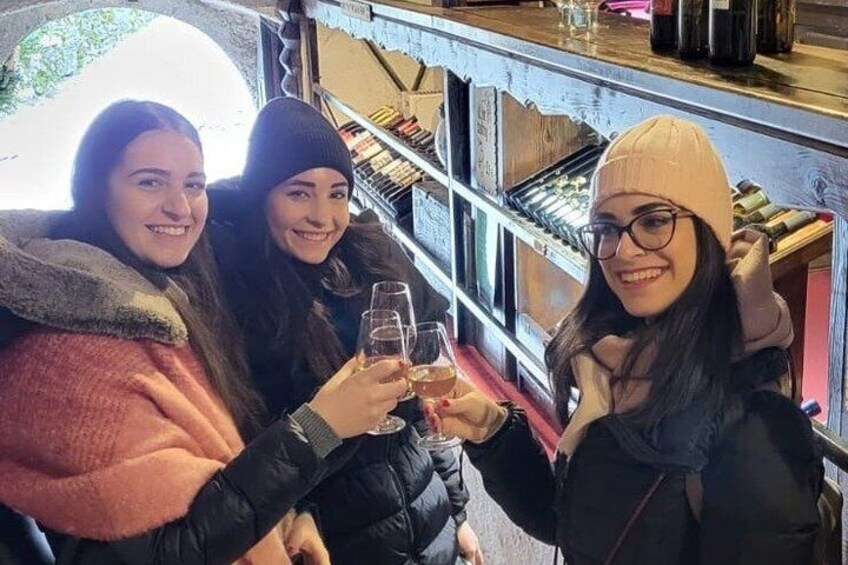 Three people toasting with drinks in a bar with shelves of bottles. 4
