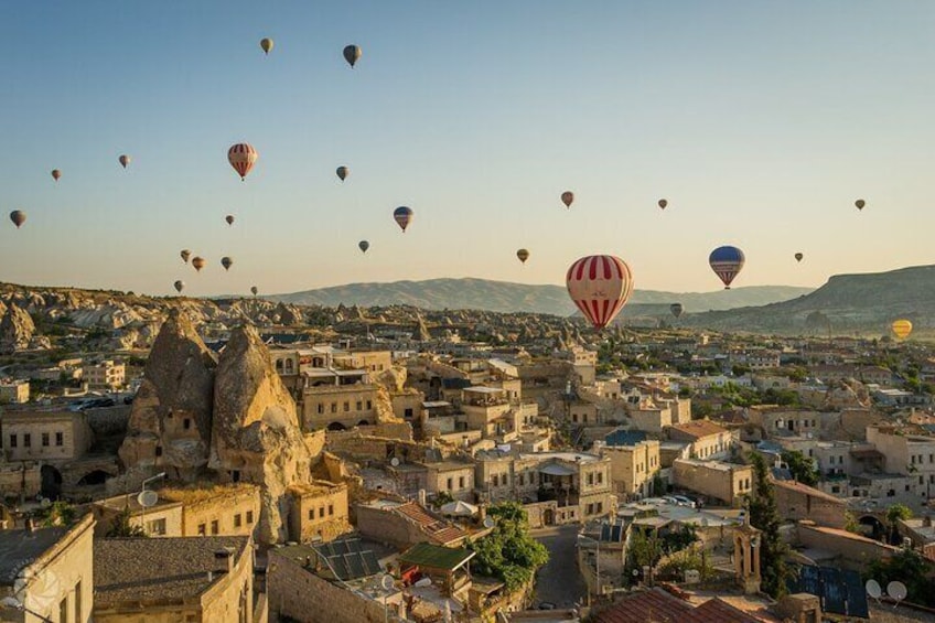 A cityscape with numerous hot air balloons in the sky, rocky formations, and traditional architecture. 1