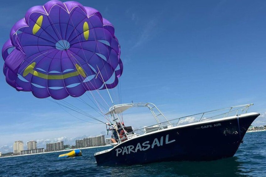A parasail with a purple canopy over a boat named 'PARASAIL' on the water. 1