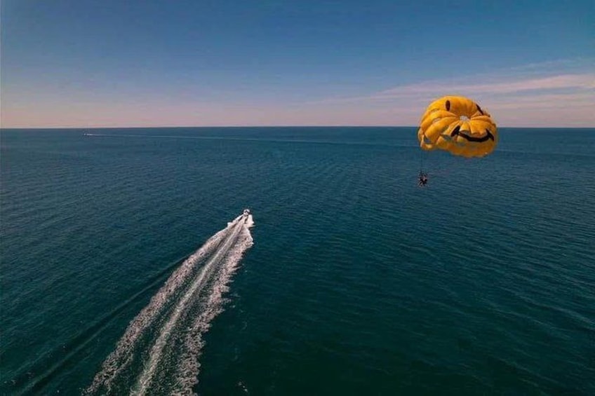 A boat with a wake, a parachute, and a person skydiving. 3