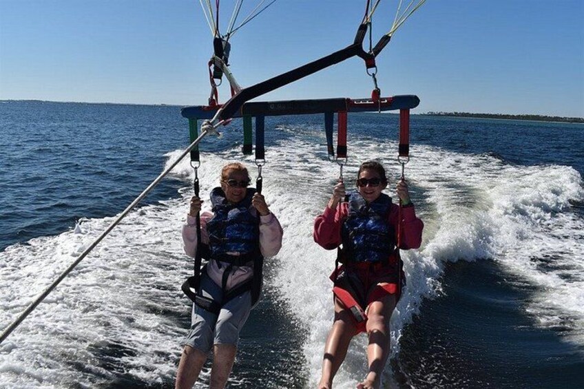 Two people on a water sport activity, holding onto a bar, with a body of water and a distant shoreline in the background. 4