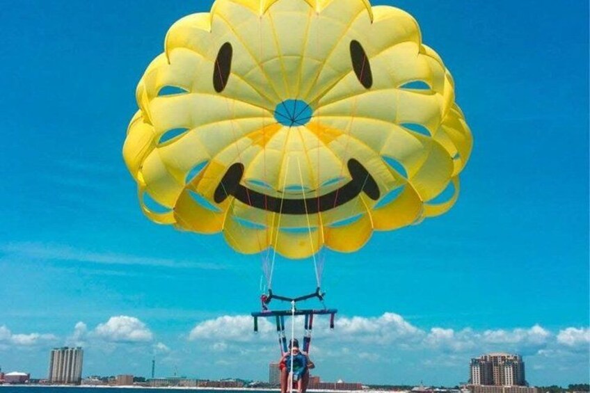 A person parasailing with a large yellow parachute against a clear blue sky. 2