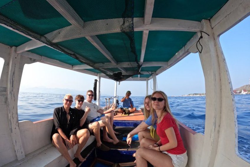 A boat with people sitting on the deck, a blue tarp overhead, and water in the background. 3