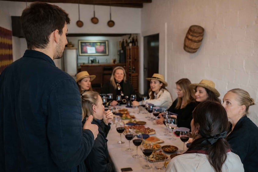 A group of people seated around a long table with wine glasses, plates of food, and a television in the background. 2