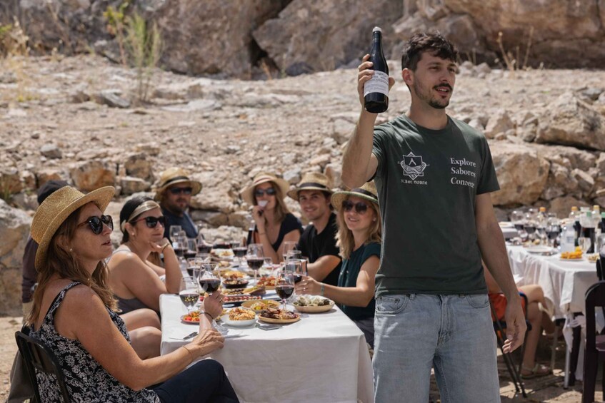 A group of people dining outdoors with a man holding a bottle of wine. 3