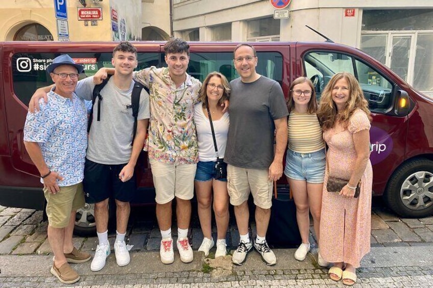 A group of people posing in front of a red van with a building in the background. 3