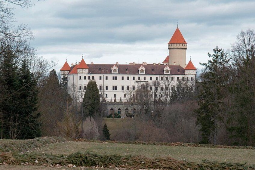 A large castle with multiple towers and a red roof, surrounded by trees and a grassy field. 4