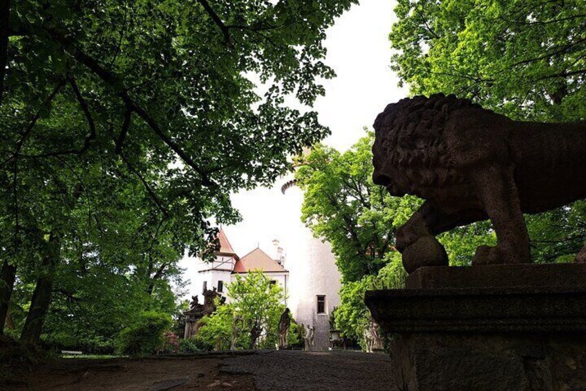 A stone lion statue in a park with trees and a building in the background. 4