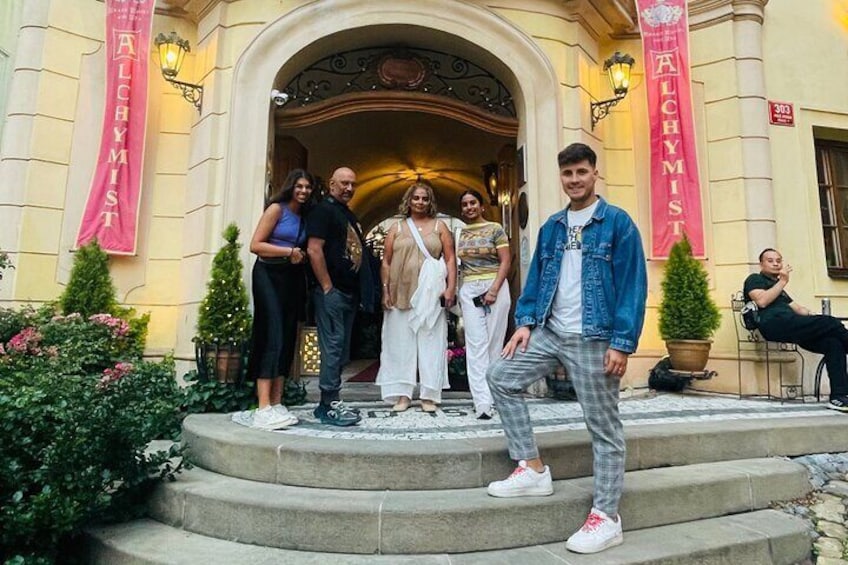 A group of people standing on a staircase in front of a building with a sign reading 'ALCHYMIST.' 2