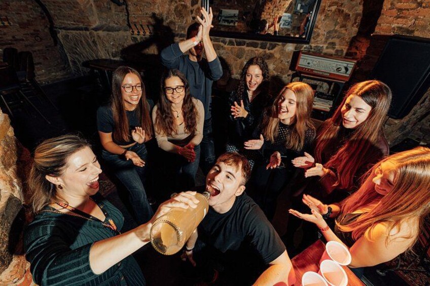 A group of people in a dimly lit room with stone walls, engaged in a social gathering. 2