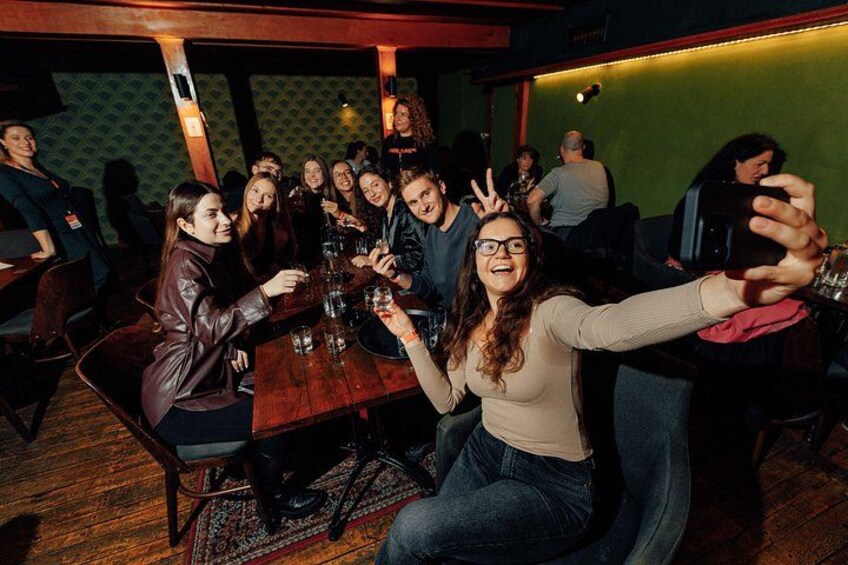 A group of people sitting around a wooden table in a dimly lit room with patterned wallpaper. 2