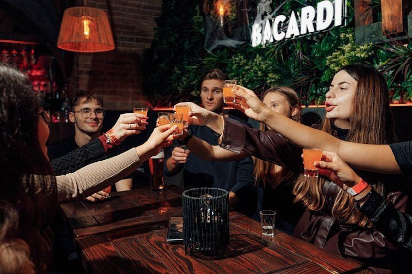 A group of people toasting with drinks in a bar with a 'BACARDI' sign in the background. 2